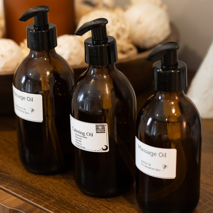 Three amber pump bottles of massage and calming oil beside a bowl of dried flowers
