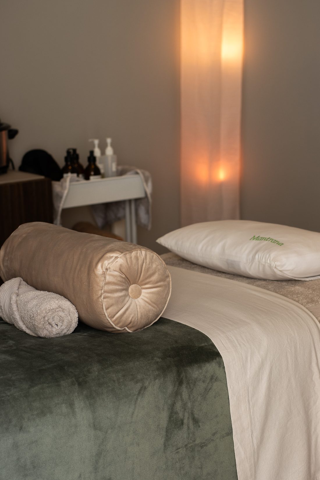 The treatment bed at Mantrana Wellness, made up with a sage velvet throw, a bolster and a Mantrana pillow, lit by a soft lamp