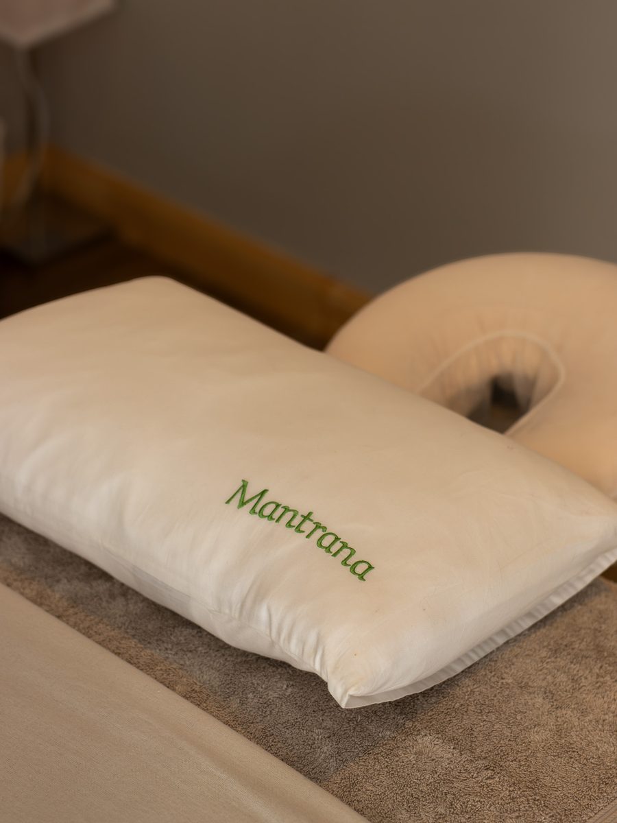 A white pillow embroidered with Mantrana in green on the treatment bed