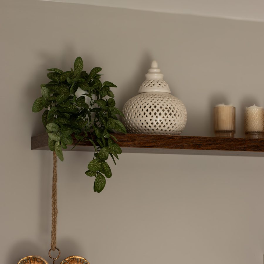 A trailing plant, a pierced ceramic lantern and candles on a shelf, with a hammered copper heart below