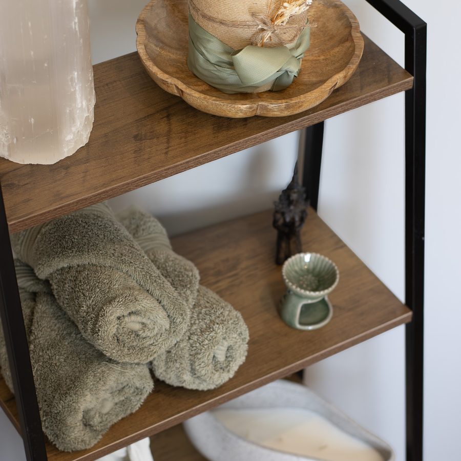 Rolled sage towels, a candle and a ceramic oil burner on wooden shelves